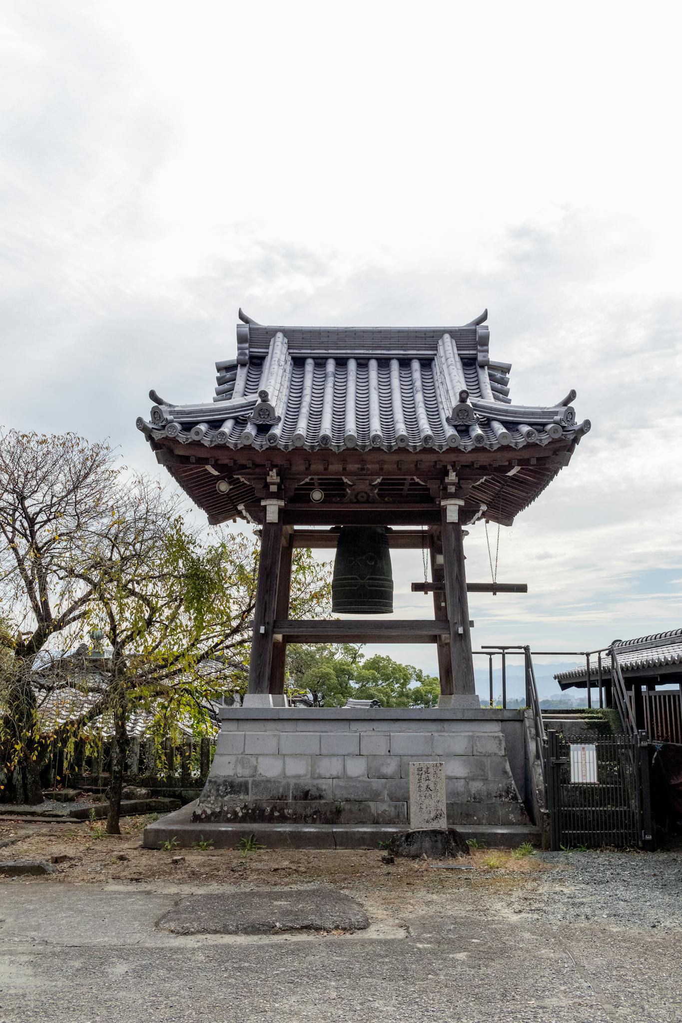 A serene view of a traditional Japanese temple bell tower under a cloudy sky, embodying cultural heritage.
