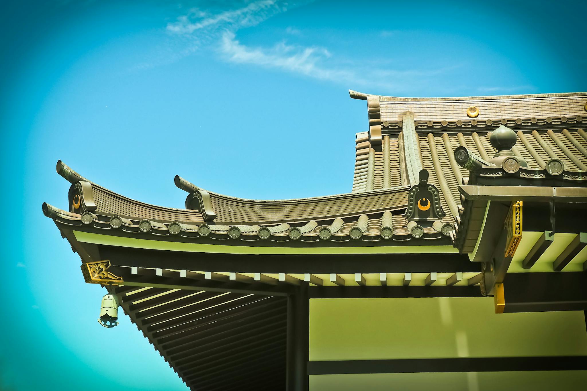 Elegant view of a Japanese temple roof displaying traditional architectural features under a bright blue sky.